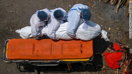 Členové rodiny a pracovníci sanitky s ochrannými pomůckami nesou tělo oběti, která zemřela na koronavirus Covid-19 na místě kremace v Novém Dillí 27. dubna 2021.