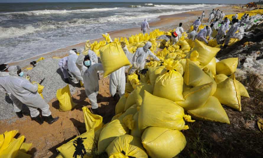 Pracovníci srílanského námořnictva na sobě čisticí zařízení na pláži se žlutými taškami naplněnými troskami