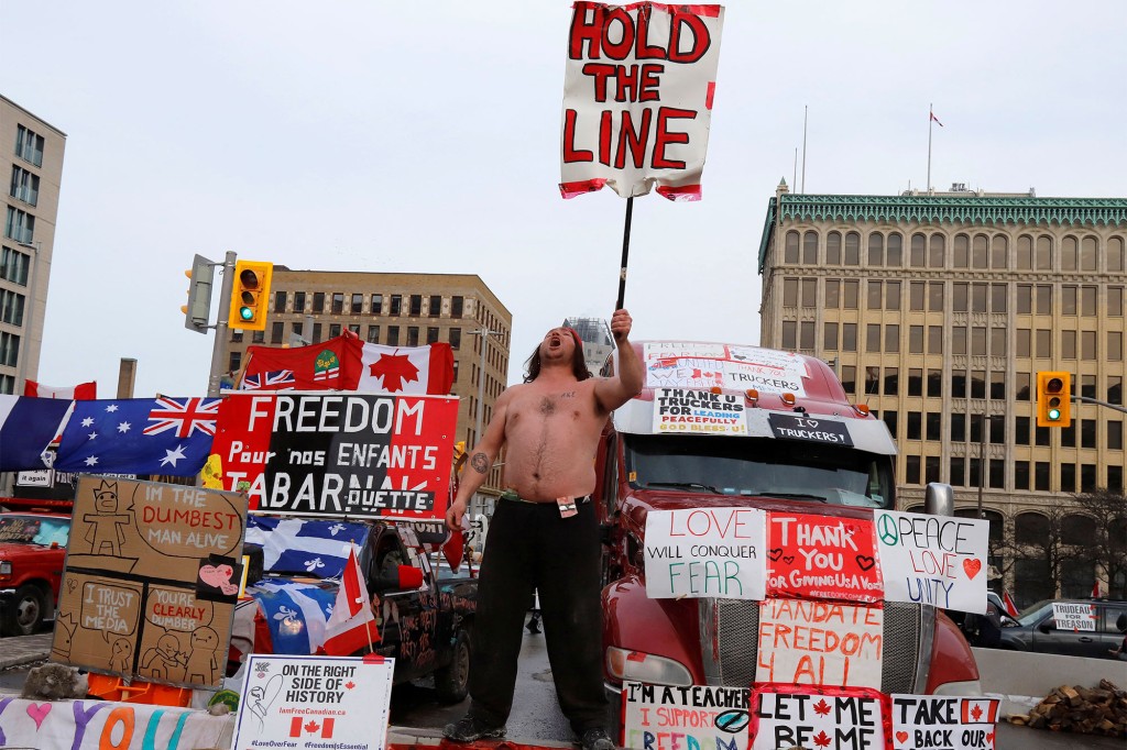 Člověk drží ceduli před kamiony blokujícími ulici v centru města, zatímco řidiči kamionů a jejich příznivci pokračují v protestech proti mandátům pro vakcínu proti koronaviru (COVID-19) v Ottawě, Ontario, Kanada.