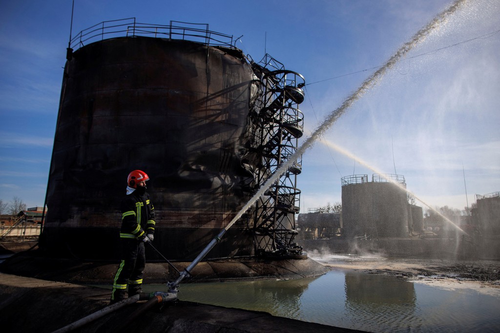 Hasiči pracují v poškozeném skladu ropy po ruském raketovém útoku na město Lvov na Ukrajině 27. března 2022.
