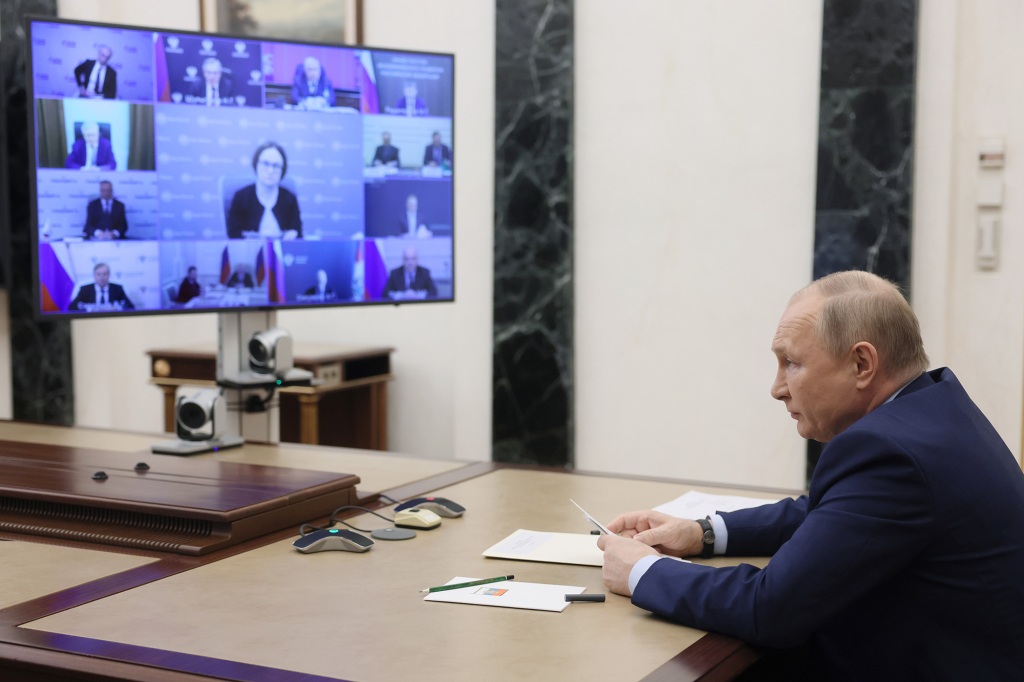 Putin sedí u stolu čelem k televizní videokonferenci.